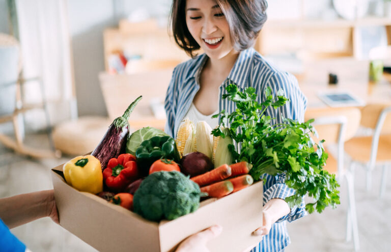 Ein Mann reicht einer asiatischen Frau einen prall gefüllten Korb mit Obst und Gemüse