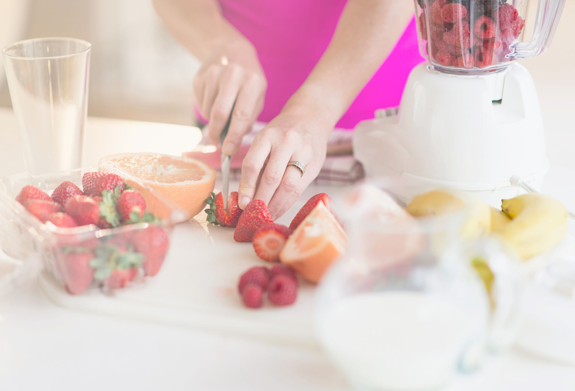 Eine Frau schneidet Erdbeeren und anderes Obst für die Zubereitung eines Smoothies im Mixer.