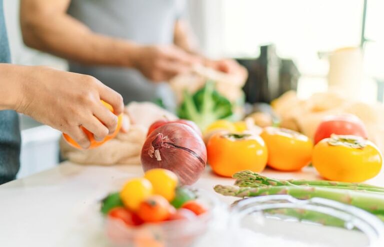 Hände, die Gemüse fürs Kochen vorbereiten.
