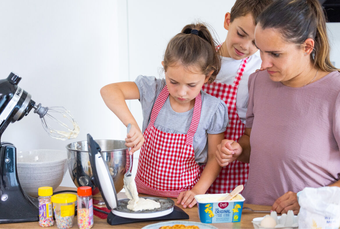 Eine Frau bereitet gemeinsam mit ihren Kindern Waffeln zu.