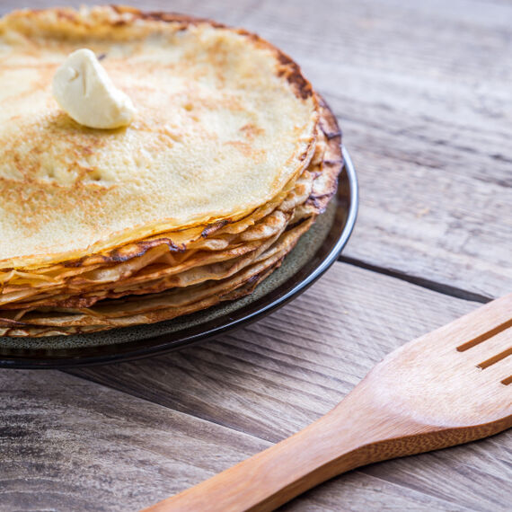 Ein Teller mit gebackenen Pfannkuchen und einem Klecks Margarine steht auf einem Holztisch