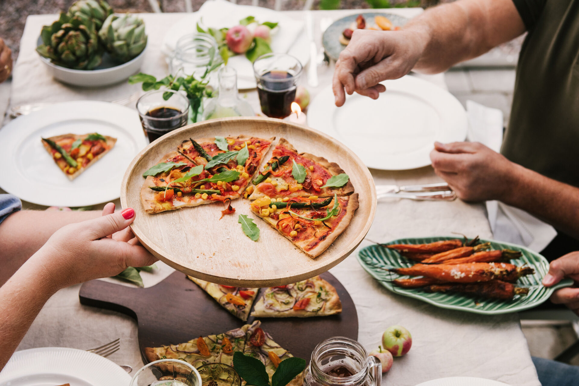 Ein gedeckter Tisch mit selbstgemachter Pizza und anderen Lebensmitteln, an denen sich mehreren Menschen bedienen.