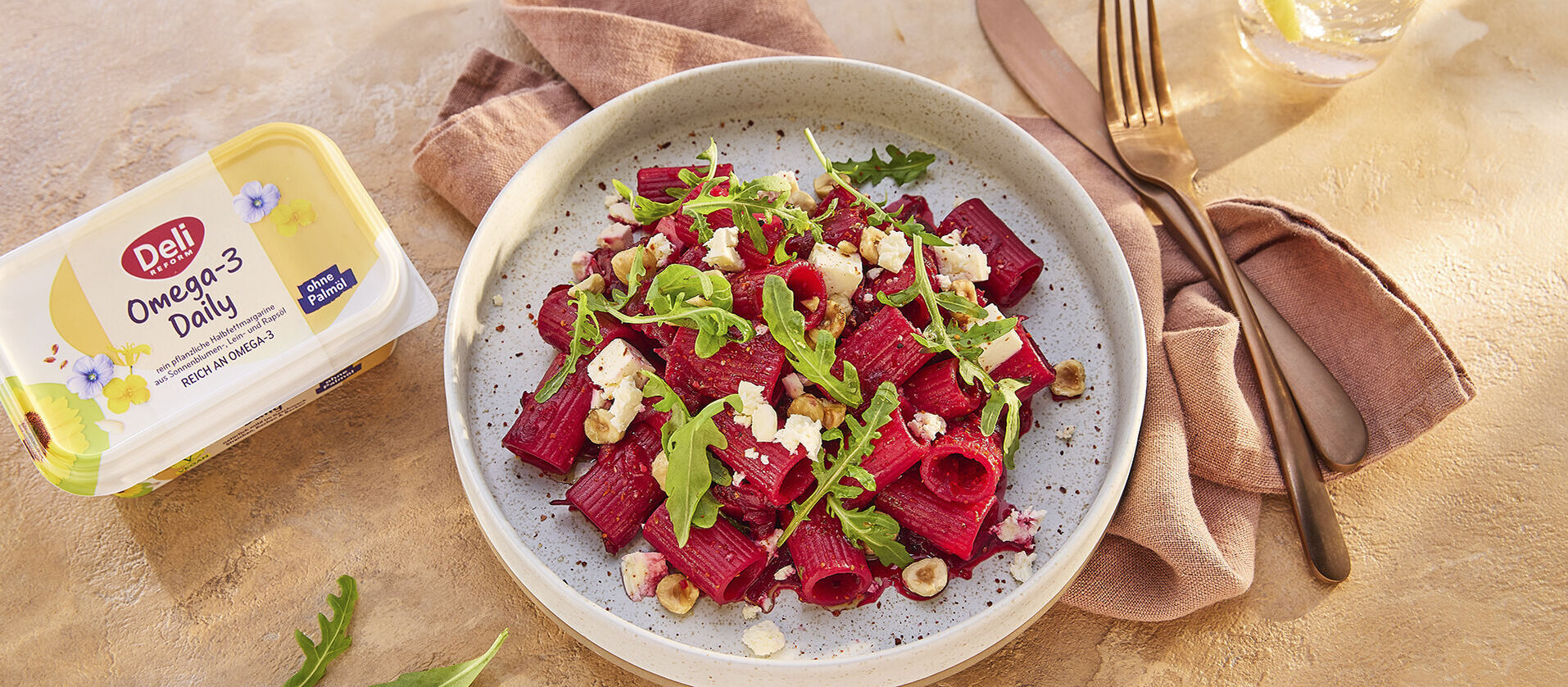 Rote-Bete-Pasta mit Rucola, Käse und Nüssen, daneben eine Packung Deli Omega-3 Daily.