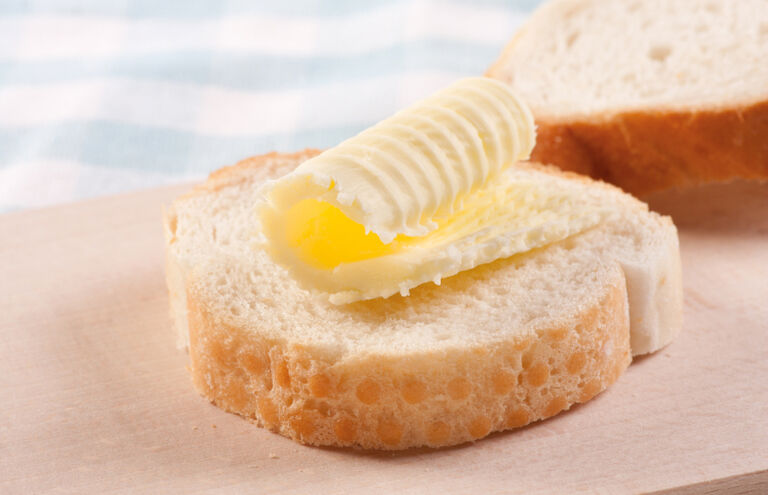 Geschnittenes Baguette auf einem Holzbrett, eine Scheibe ist mit Margarine bestrichen