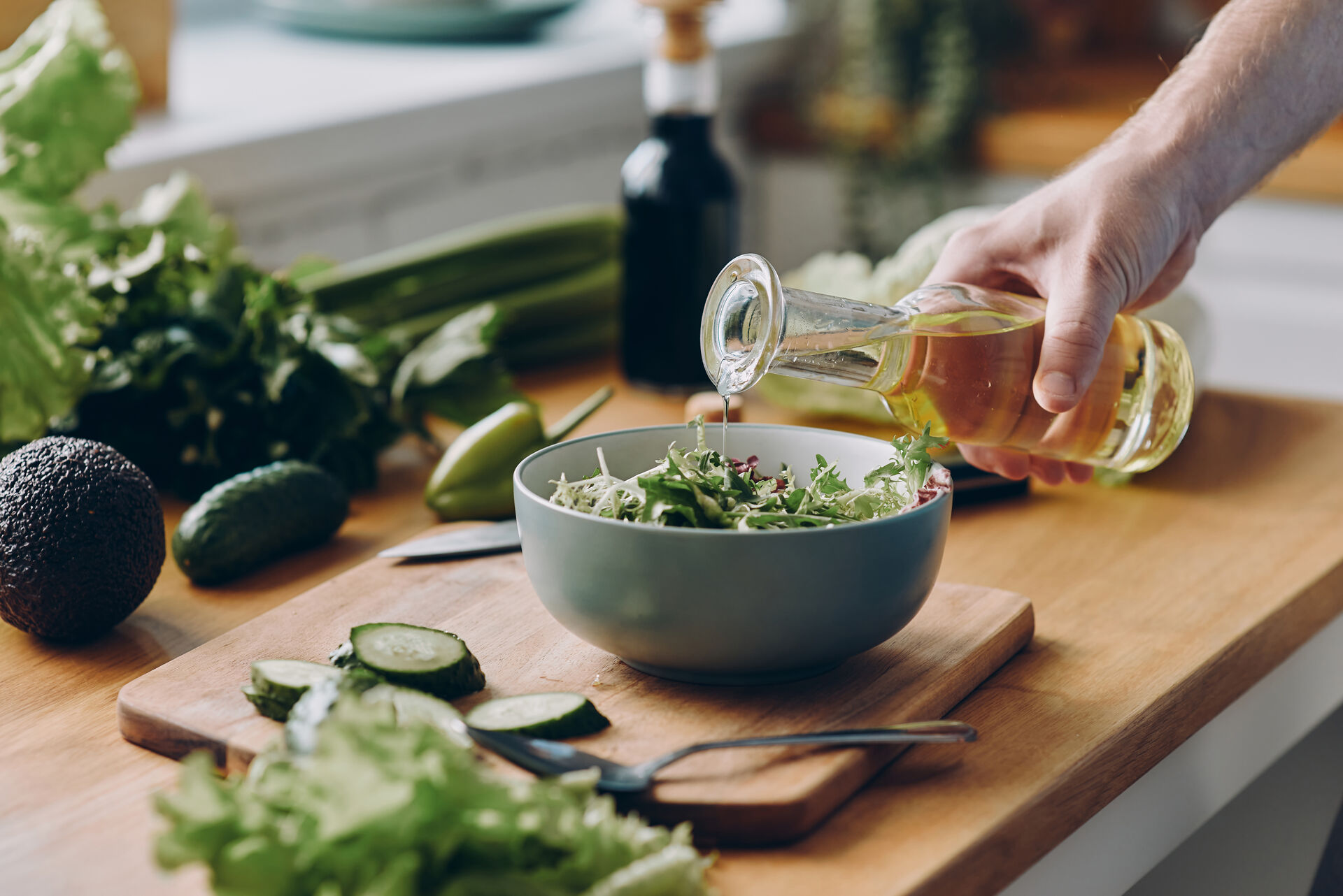 Eine Hand, die Pflanzenöl über einen frischen Salat gießt