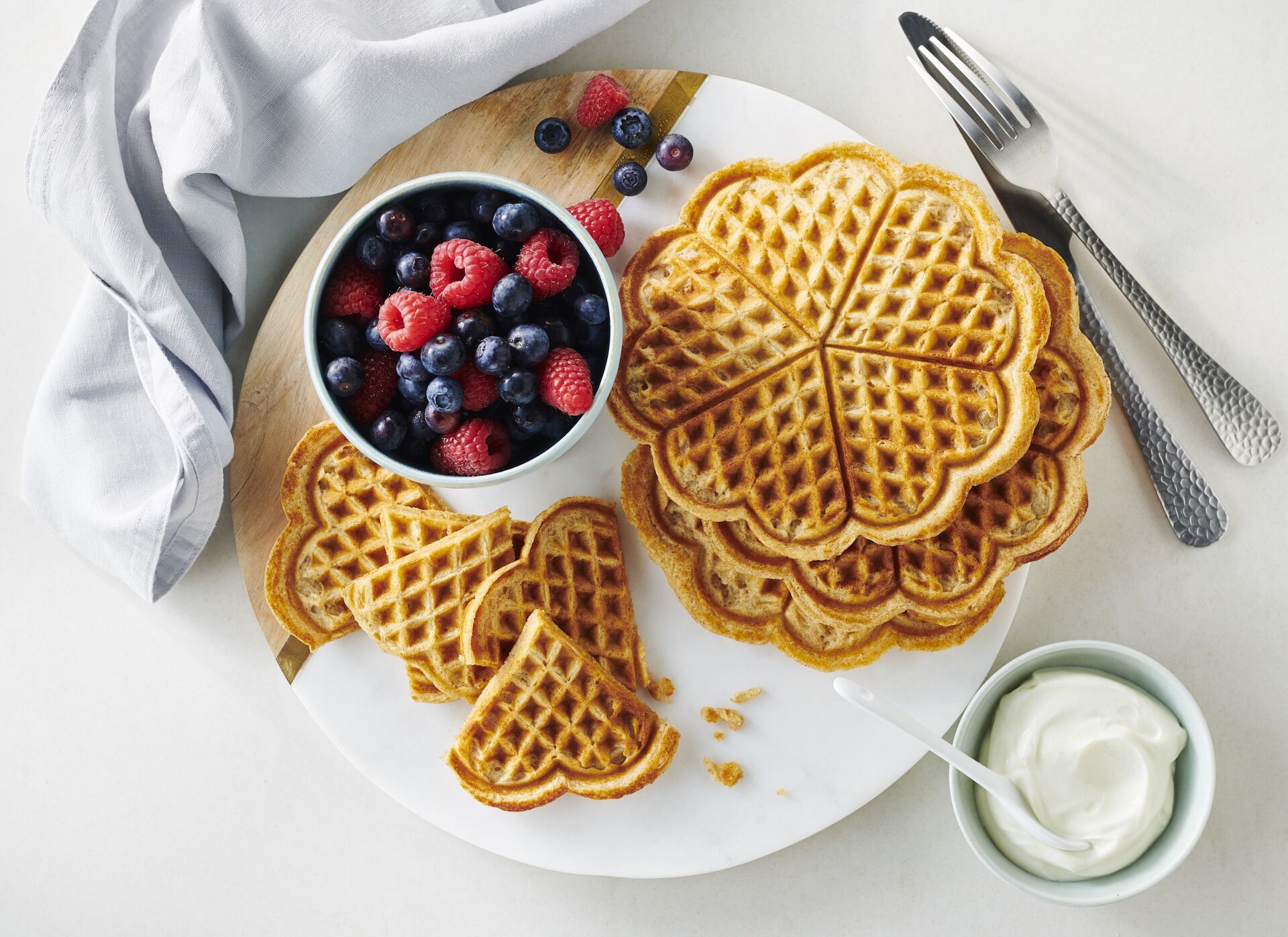 Auf einem Teller liegen frisch gebackene Waffeln neben einer Schüssel mit Himbeeren und Blaubeeren. 