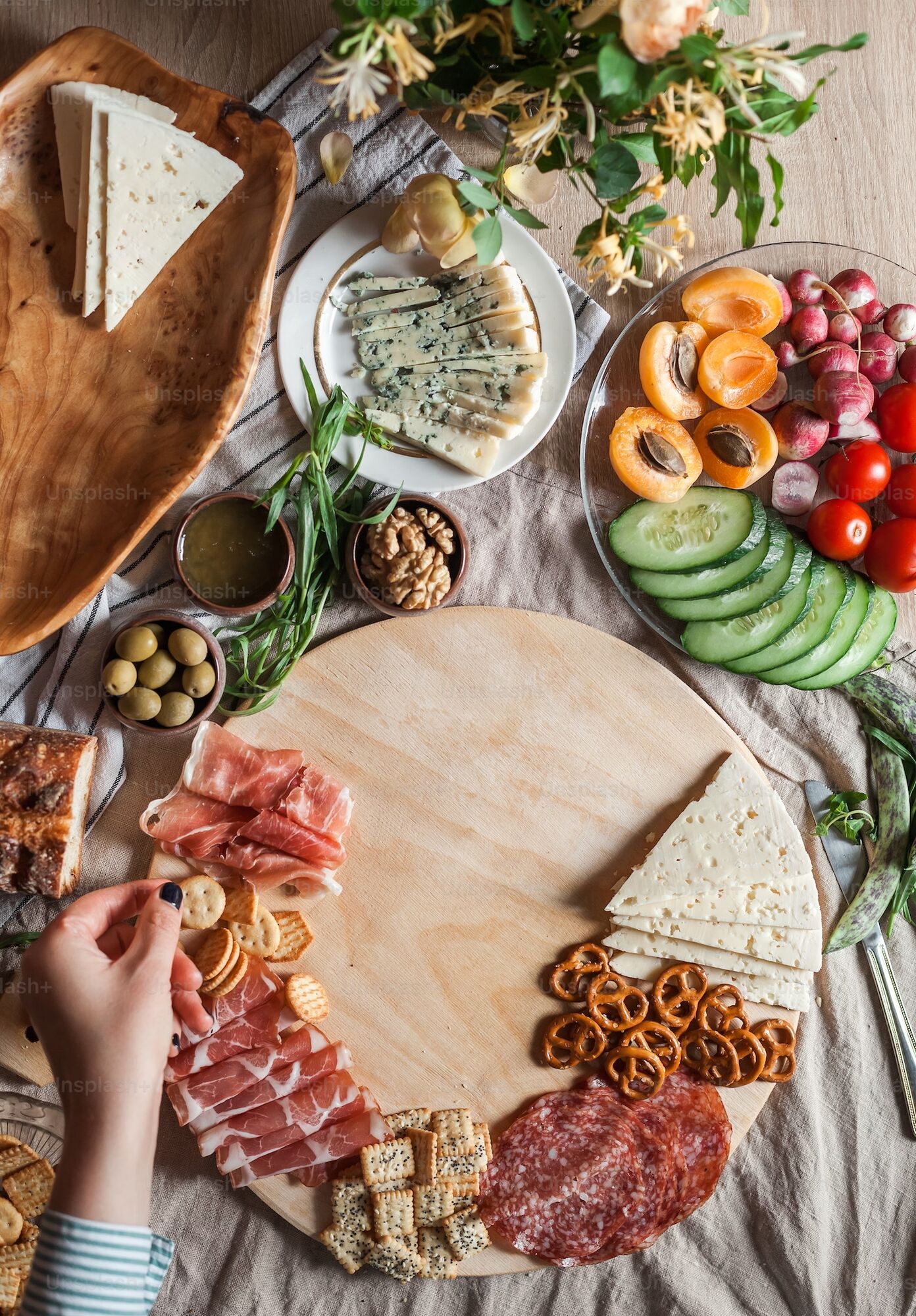 Eine Frau belegt ein Charcuterie-Board mit Käse, Räucherschinken, Aufschnitt und Crackern.