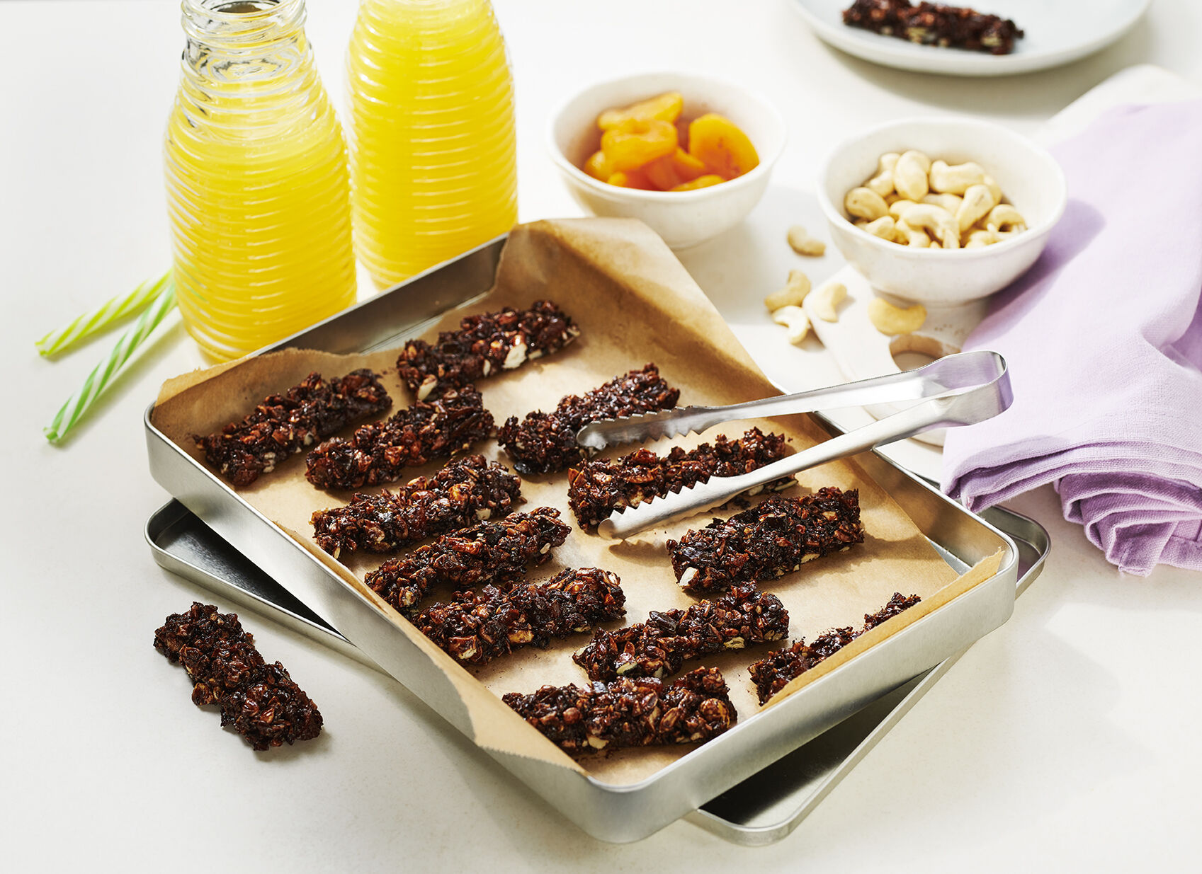 Auf einem Backblech mit Backpapier liegen gebackene Sticks aus Aprikosen und Cashewkernen.