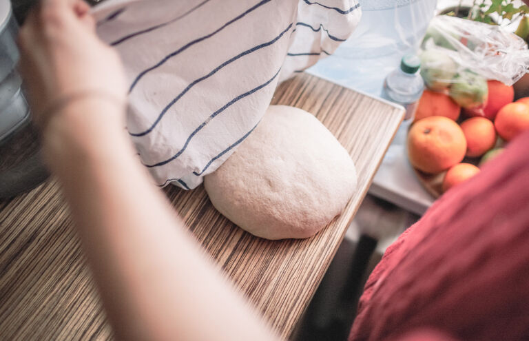 Hände, die ein Handtuch über Brotteig auf einem Tisch legen