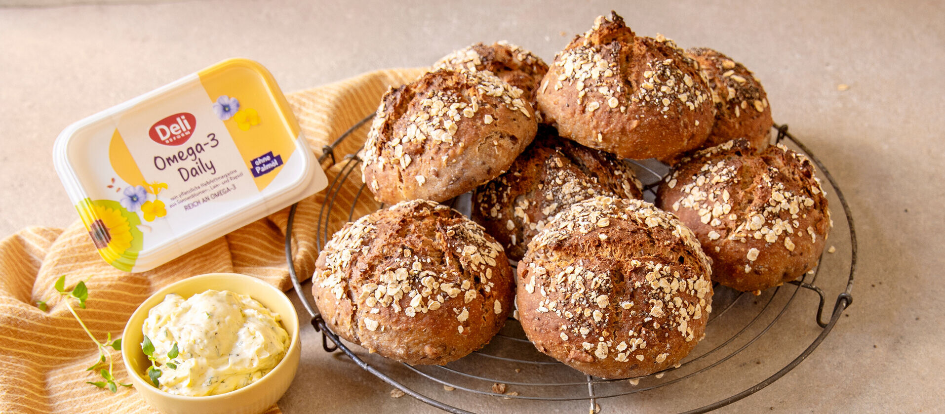 Quarkbrötchen mit Haferflocken auf einem runden Gitter, daneben ein aufgeschnittenes Brötchen mit Zitronen-Thymian-Aufstrich