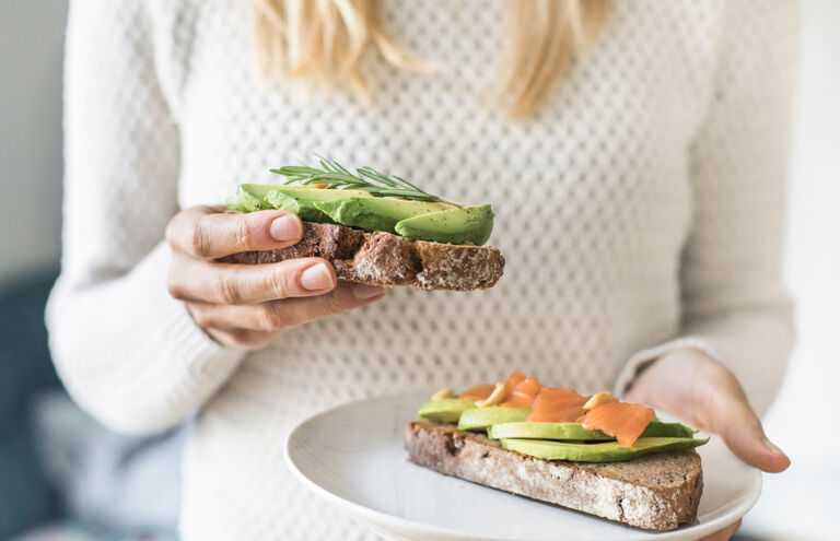 Frau hält Teller mit Brotscheiben, die mit Avocado und Räucherlachs belegt sind.