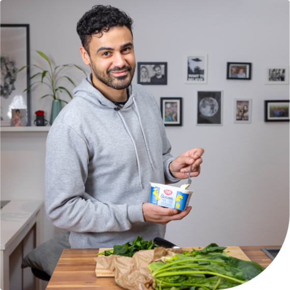 Ein junger Mann hält eine Margarinepackung und vor ihm liegt Gemüse, um besser zu essen