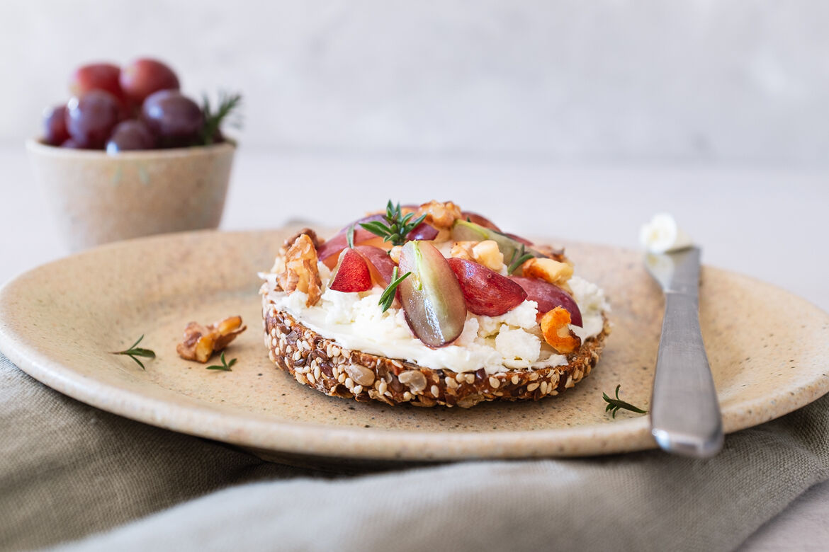  Nahaufnahme von einem Butterbrot, belegt mit Ziegenfrischkäse, Weintrauben und karamellisierten Walnüssen 