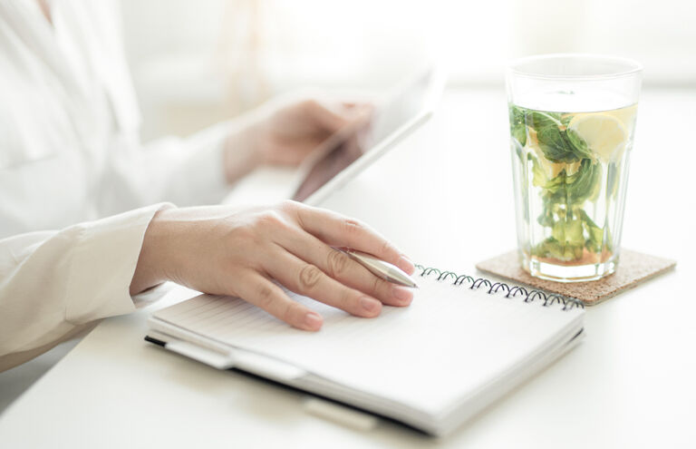 Frauenhände halten Stift und Tablet am Schreibtisch mit Glas mit frischem Minztee