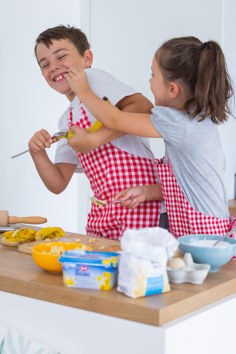 Ein Junge und ein Mädchen mit karierten Schürzen haben Spaß beim gemeinsamen Backen.